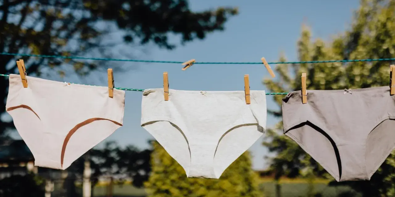 Drei Unterhosen in verschiedenen Grautönen trocknen an einer Wäscheleine. Das Bild zeigt den Prozess des Unterhosen waschen.