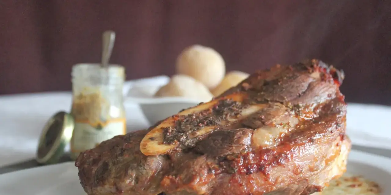Costilla de ternera asada jugosa con hueso, servida en plato blanco con salsa y guarnición.