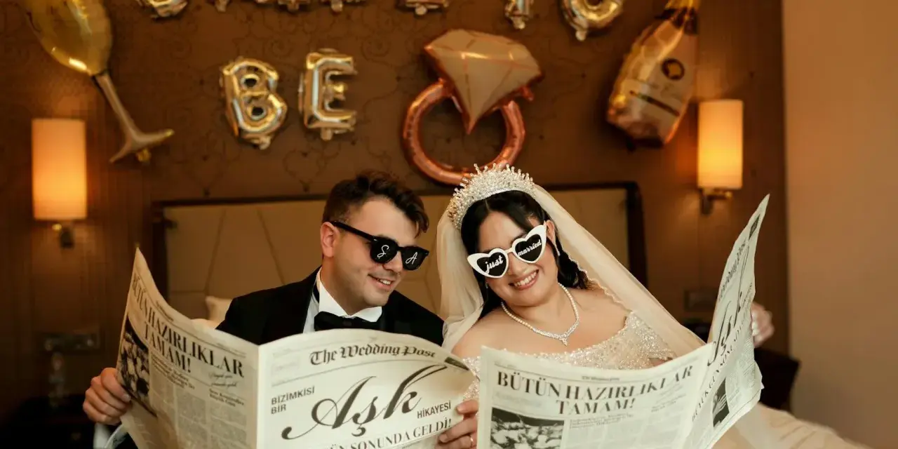 Para Młoda czyta gazetę z nagłówkiem "przykładowy harmonogram wesela". Balony "Bride to be" i kieliszek szampana w tle.