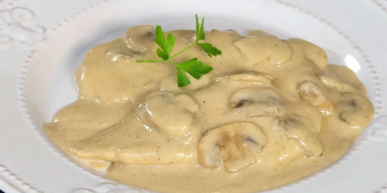 Pollo cremoso con champiñones y perejil en un plato blanco.