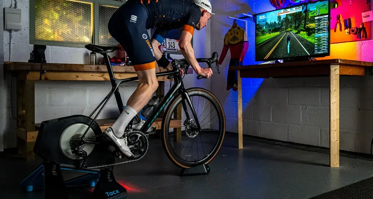 Cyclist on a Tacx trainer, connected to a TV displaying a Zwift course. This setup showcases Zwift compatible devices for an immersive indoor cycling experience.