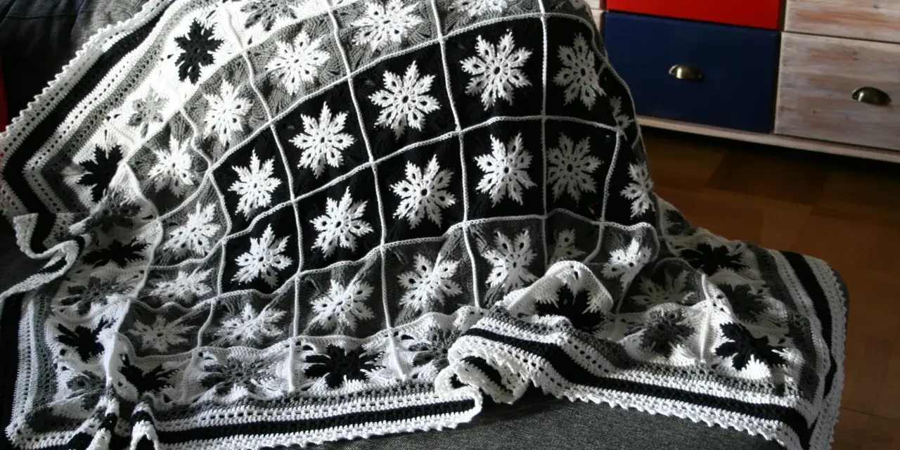 En virkad pläd med mormorsrutor i svart, vitt och grått. Snöflingemönstret är vackert och detaljerat.