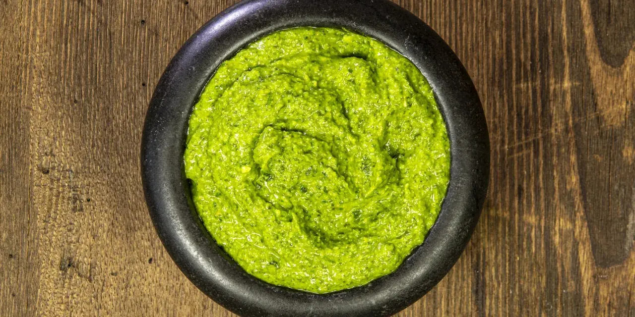Pesto genovese ricetta originale in un mortaio di pietra, su un tavolo di legno rustico. Fresco e profumato.