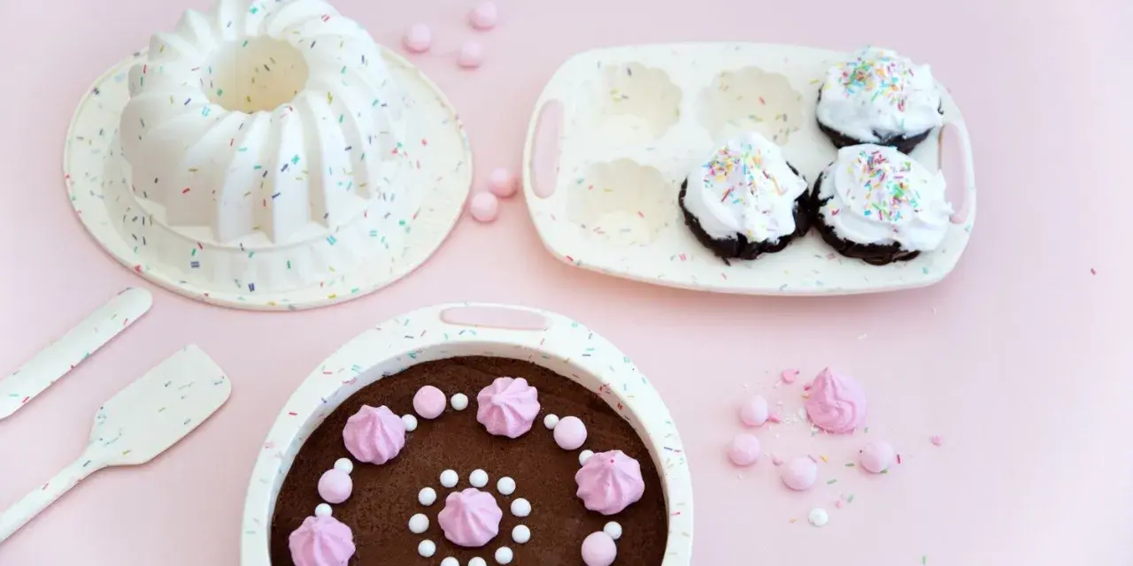 Förberedelser för ett härligt baka kalas! En sockerkaksform, muffinsform och en färdig chokladkaka med rosa maränger och strössel.
