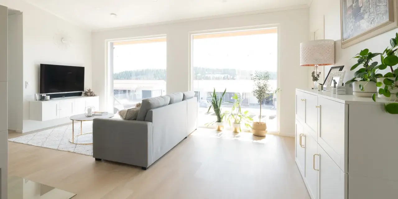 Ett ljust vardagsrum med en grå soffa, ett runt soffbord och en vit förvaringsmöbel. En lampa med vitt ljus lyser upp rummet.
