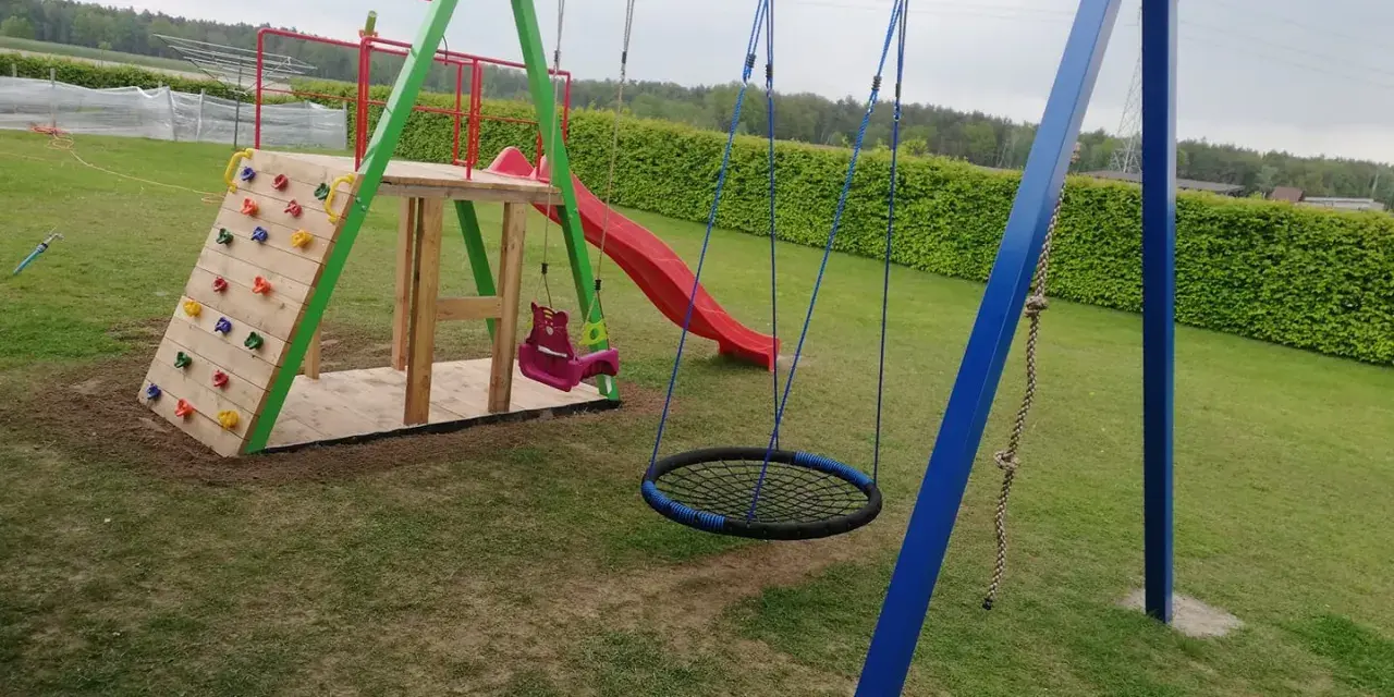 Plac zabaw z wspinaczką, zjeżdżalnią, huśtawkami i okrągłą huśtawką.