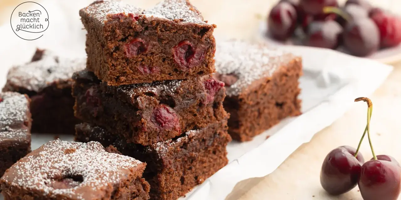 Saftige Stücke von Omas Schoko-Kirsch-Kuchen, bestäubt mit Puderzucker. Kirschen sind im dunklen Teig sichtbar.