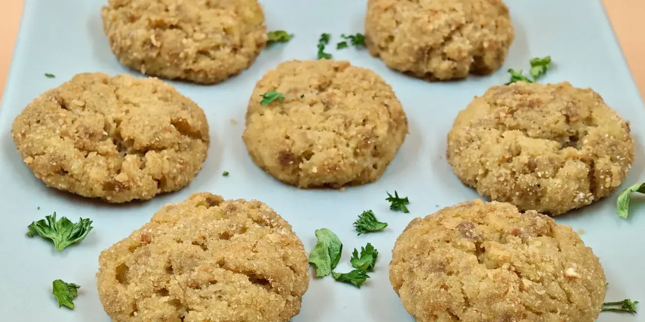 Sei polpette di patate dorate e croccanti, guarnite con prezzemolo fresco, su un piatto azzurro.