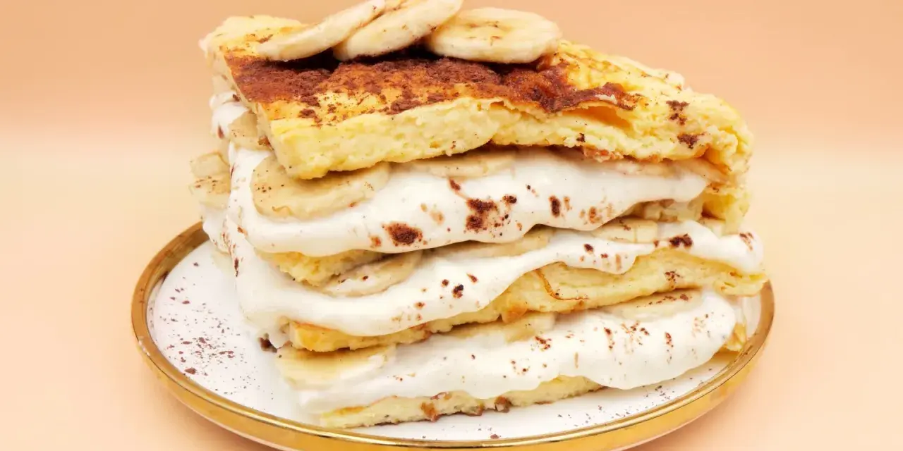 Wysoki omlet z bananem, przełożony kremem i plasterkami banana, posypany kakao. Pyszny deser na talerzyku.
