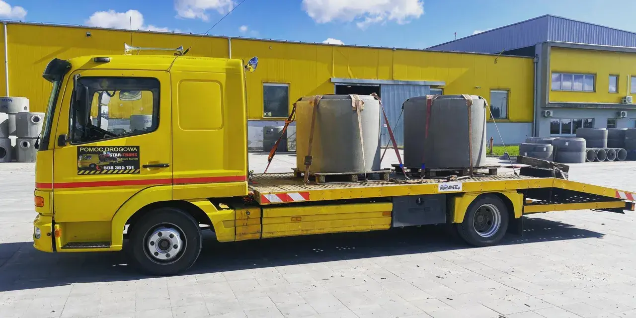 Żółta laweta z dwoma betonowymi elementami, gotowa do transportu. To **assistance warta** uwagi, gdy potrzebujesz przewieźć ciężkie ładunki.