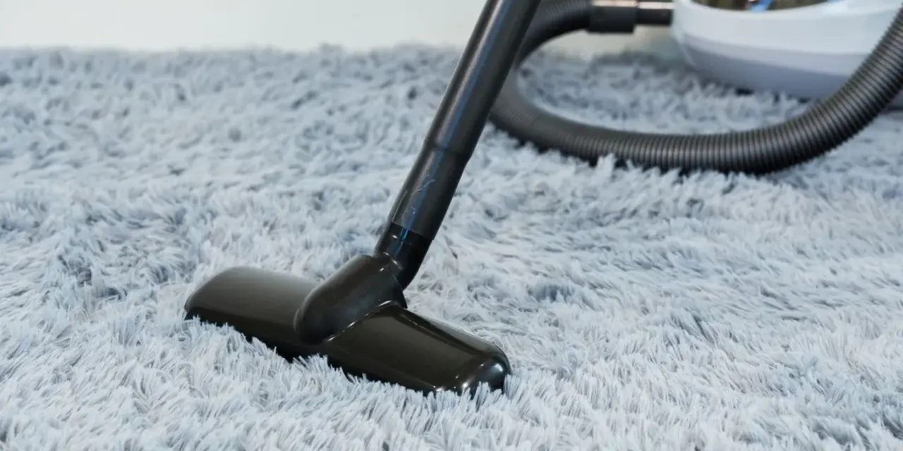 Vacuum cleaner head on a fluffy grey rug, demonstrating how to wash a rug by removing dust and debris.