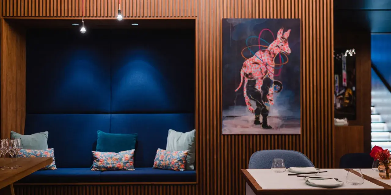 Gemütliche Nische mit blauen Kissen und einem orientalischen Teppich. Ein Kunstwerk mit einem pinken Zebra ziert die Holzwand. Ein echter Berlin Restaurant Geheimtipp.