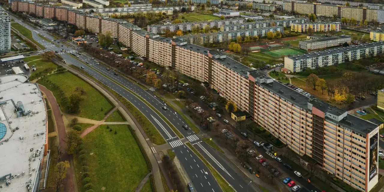 Widok z lotu ptaka na najdłuższy blok w Europie, rozciągający się wzdłuż ruchliwej drogi i otoczony zielenią oraz innymi budynkami mieszkalnymi.