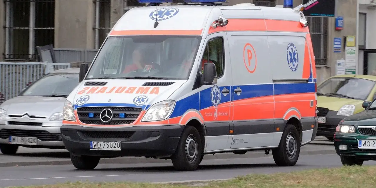 Karetka na sygnale z oznaczeniami medycznymi, jadąca ulicą.