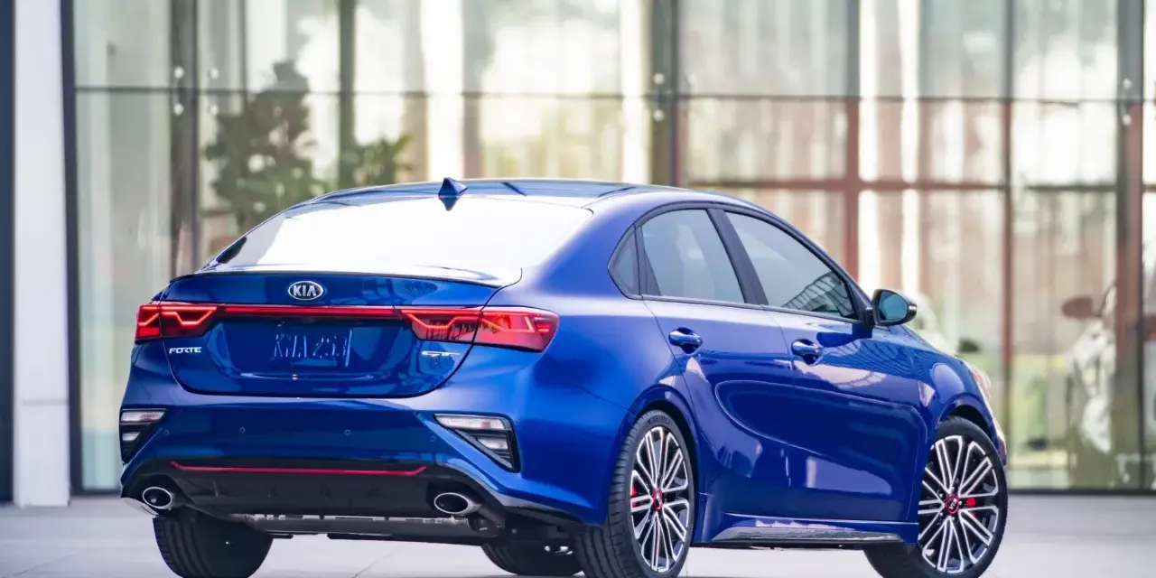Niebieski sedan Kia Forte z widokiem z tyłu, z czerwonymi akcentami i sportowymi felgami.