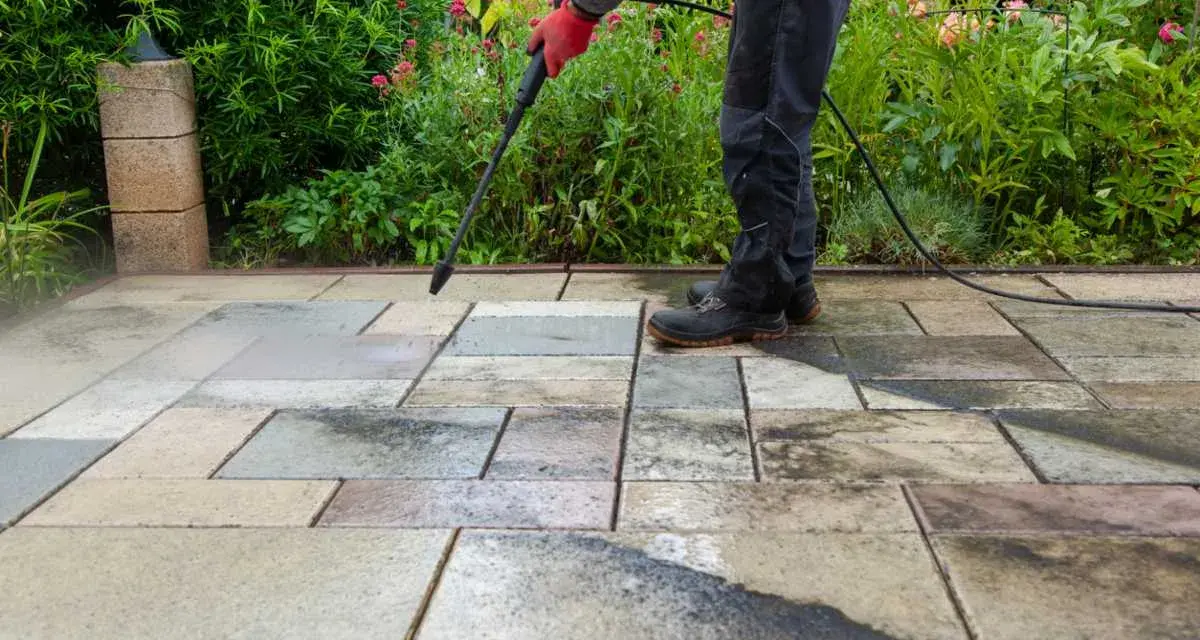 Persona con guantes rojos usa hidrolimpiadora para limpiar suelo terraza exterior.