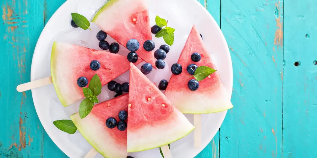 Erfrischendes Wassermelonen Eis mit Blaubeeren und Minze auf Eiswürfeln, serviert auf einem weißen Teller.