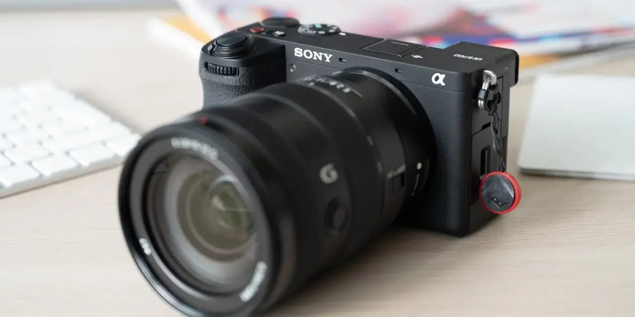 Appareil photo Sony Alpha a6700 prêt pour un test. Un objectif noir est monté, avec un clavier blanc et des documents flous en arrière-plan.