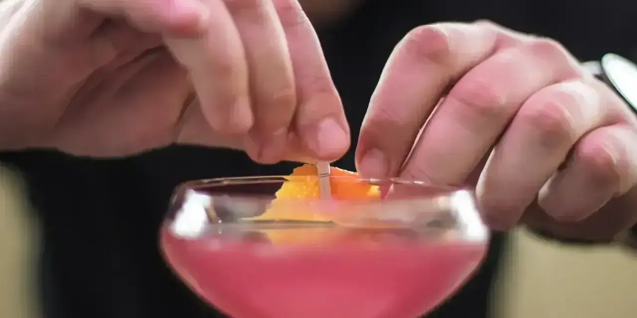 Ręce dekorują drinka skórką pomarańczy. To ostatni krok w przygotowaniu Cosmopolitan przepis.