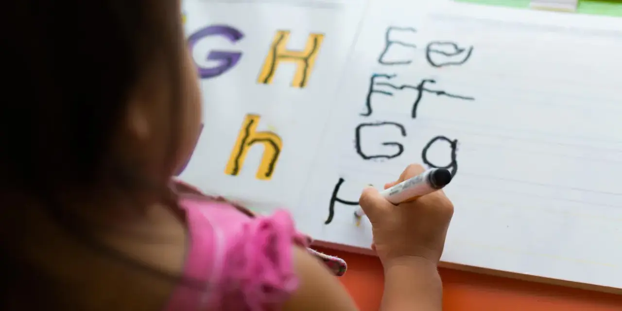 Dziecko ćwiczy łączenie liter pisanych na tablicy. Litery G, H, h, E, F, G, H.
