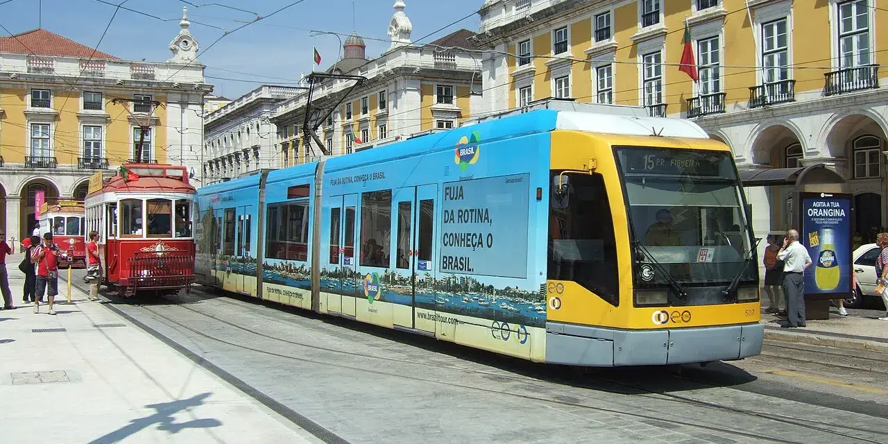 Lizbona tramwaj: nowoczesny, niebiesko-żółty pojazd obok zabytkowego, czerwonego tramwaju na tle żółtych budynków.