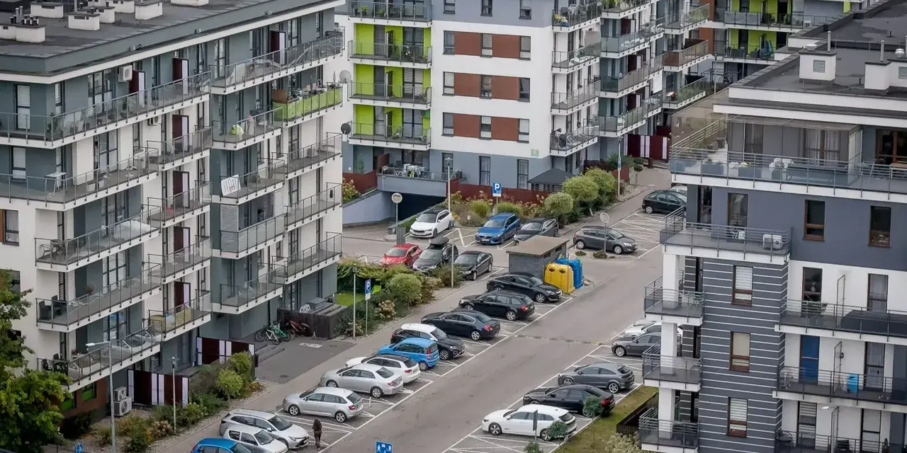 Nowy blok mieszkalny z balkonami i samochodami na parkingu. Kto musi zapłacić 64 tysiące złotych kary za uchylanie się od podatku od nieruchomości?