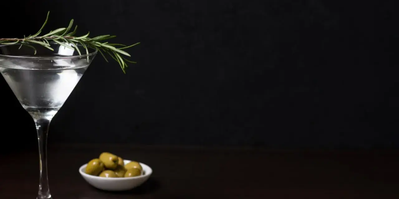 Elegancki kieliszek z drinkiem, gałązka rozmarynu i oliwki. Czy to Dirty Martini, czy klasyczne Dry Martini?