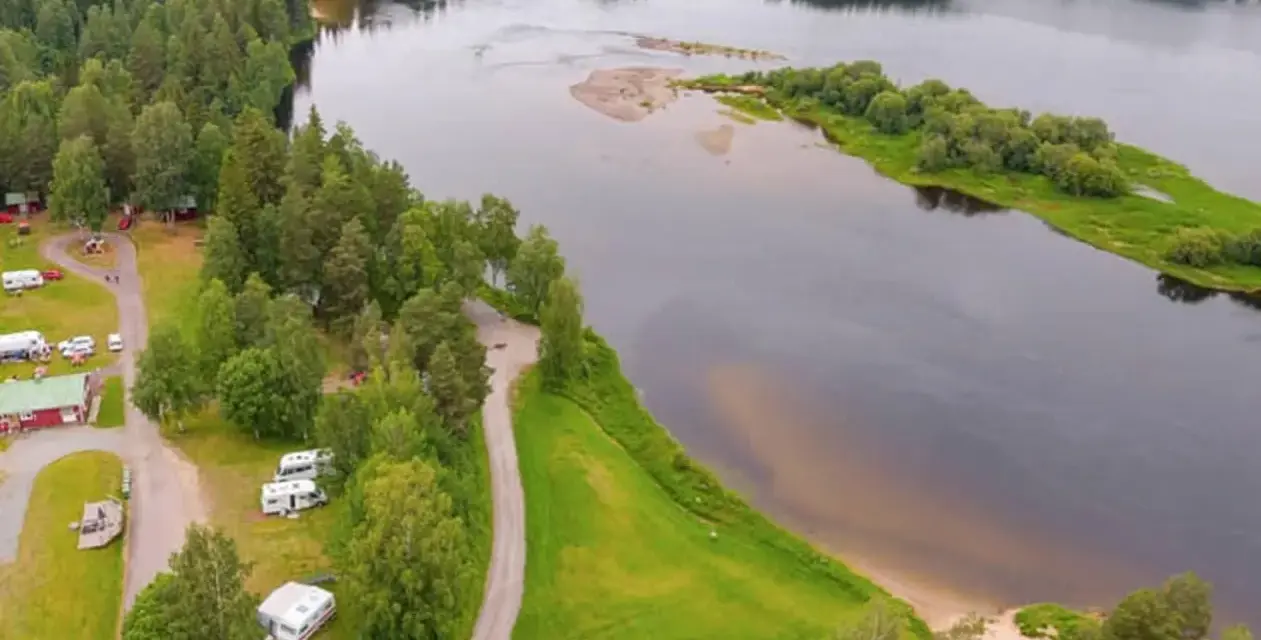 Vacker vy över Selholmens camping med husbilar och stugor vid en sjö omgiven av skog.