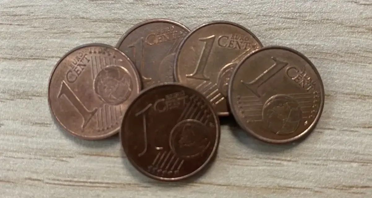 Cinq pièces de 1 centime d'euro, certaines semblant être une pièce de 1 euro rare valeur, sont disposées sur une surface en bois.