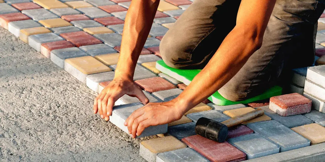 Ręce układają kolorową kostkę brukową na betonie. Powstaje równy wzór.