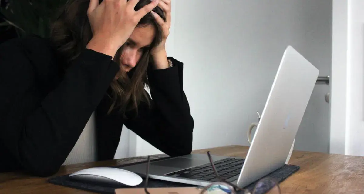 Kobieta z rękami na głowie przy laptopie, wyrażająca frustrację i myśląc o porzuceniu pracy.