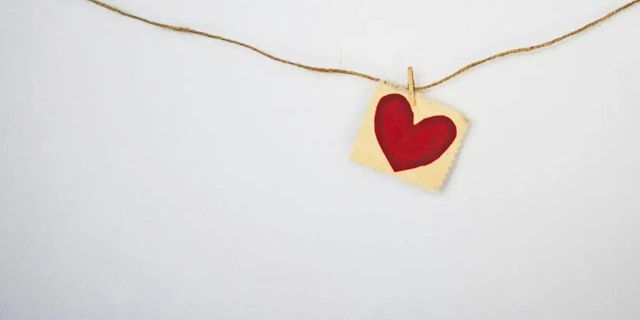 A red heart on a small fabric square, hung by a clothespin on a string. A simple symbol, asking: does God love everyone?