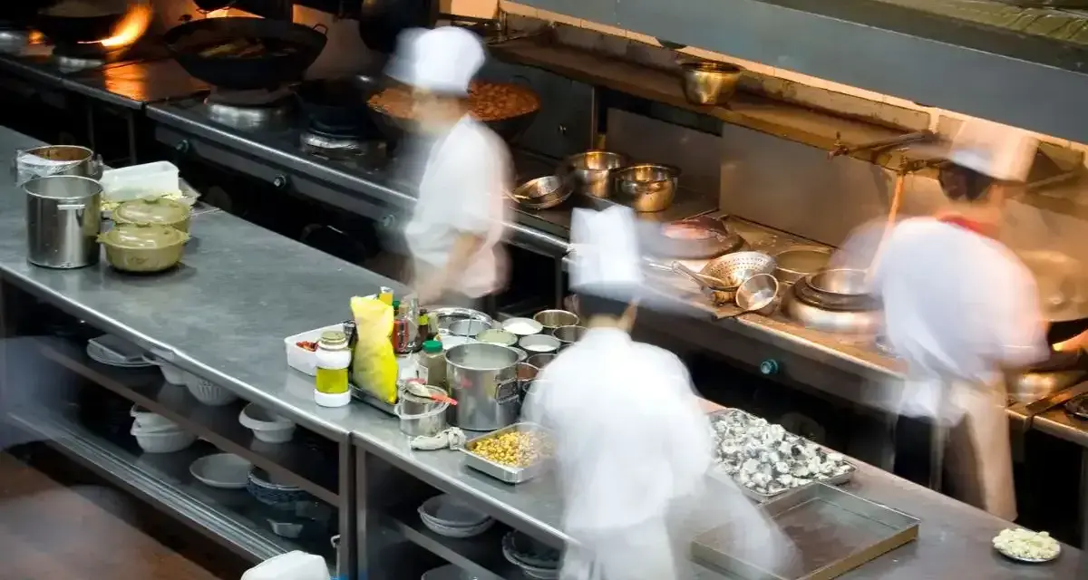 Chefs en movimiento en una cocina profesional, con ollas humeantes y ingredientes listos. El "mise en place" es clave para la eficiencia.