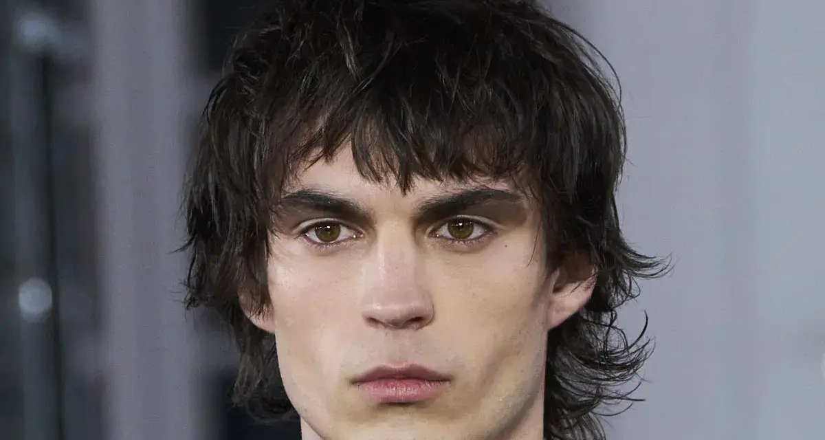 Joven con un corte de pelo mullet desordenado, mirada intensa y cejas marcadas.