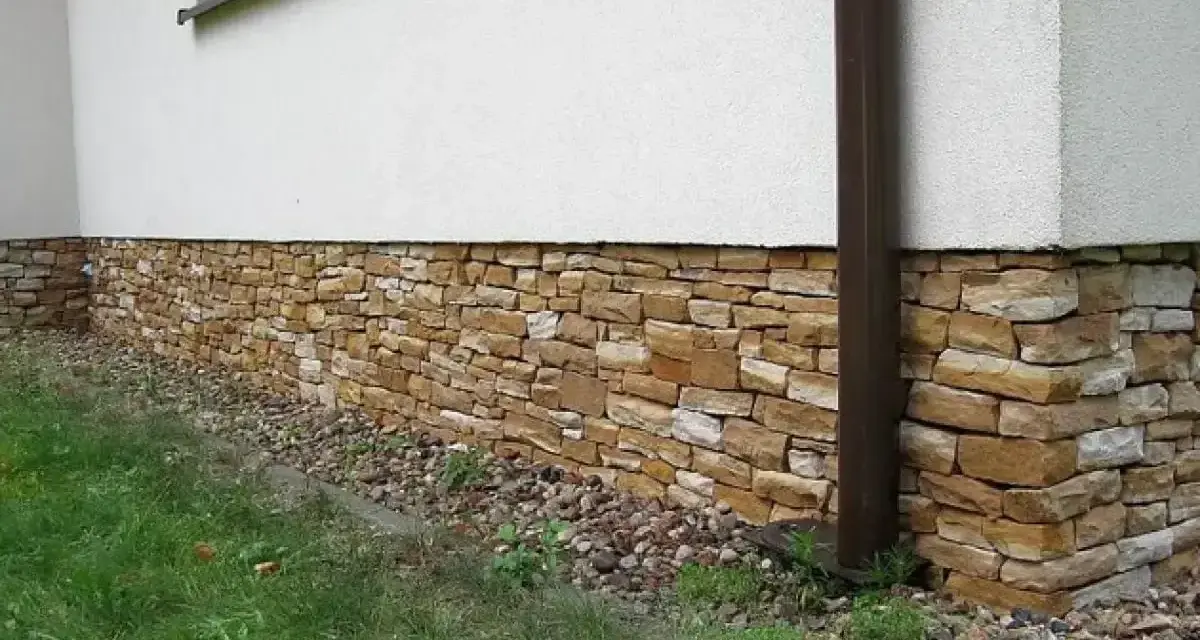 Eleganckie cokoliki z kamienia ozdabiają dom, tworząc naturalną, kamienną opaskę wokół białej ściany.