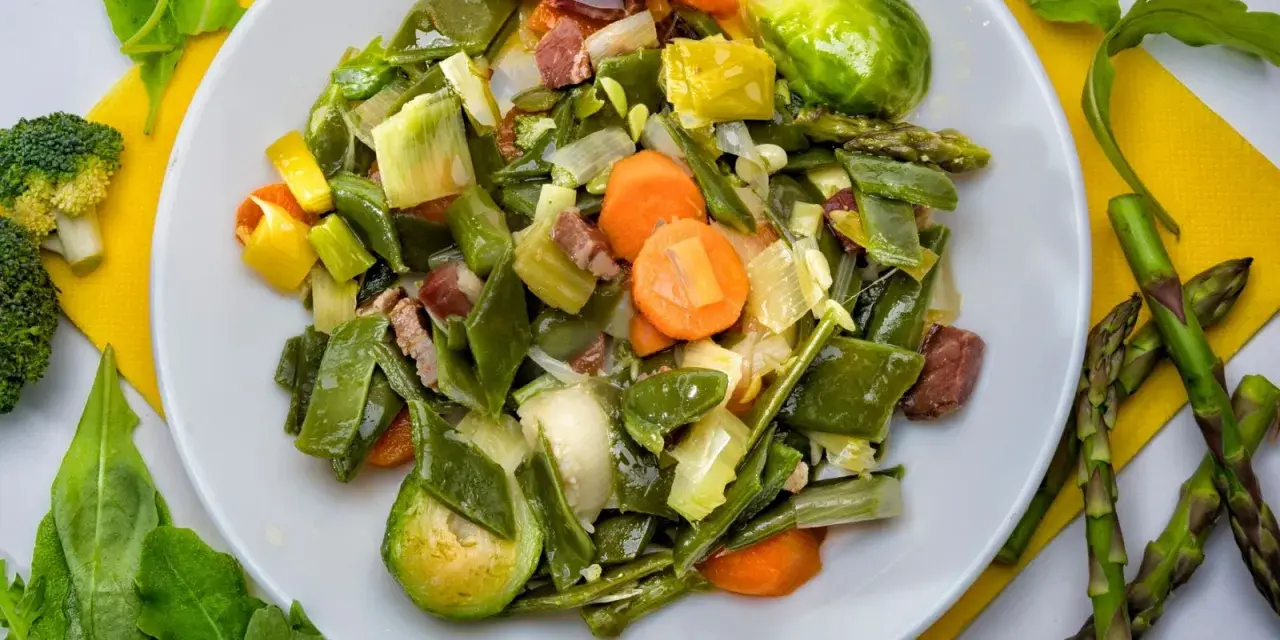 Menestra de verduras variadas con trozos de jamón en un plato blanco.
