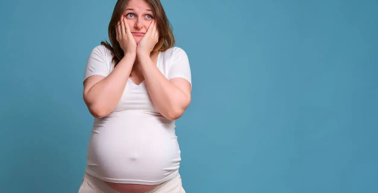 Donna incinta con le mani sul viso esprime paura in gravidanza, preoccupata per il futuro.