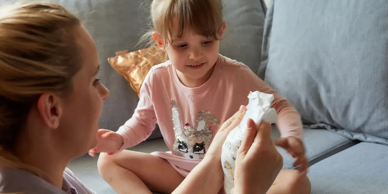 Mama pokazuje córce pieluchę, symbolizując etap, kiedy dziecko przestaje nosić pieluchy.