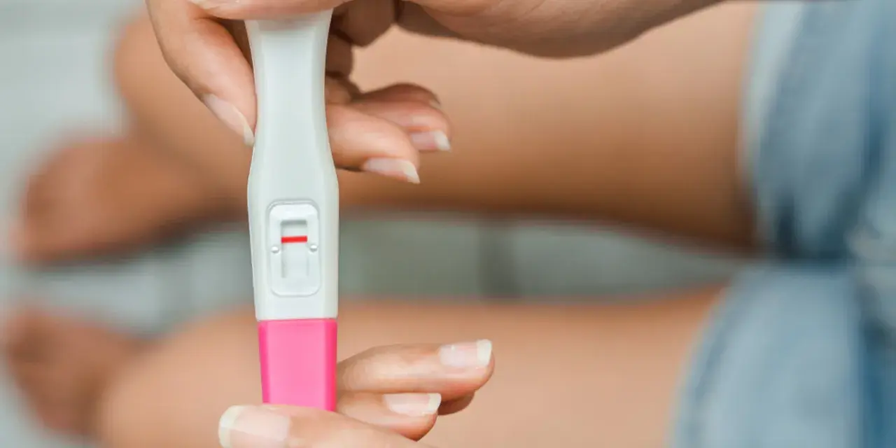 Dłoń trzyma test ciążowy z jedną czerwoną kreską. Kiedy zrobić test ciążowy? Najlepiej po terminie spodziewanej miesiączki.