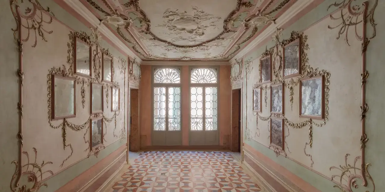 Corridoio decorato con stucchi dorati e specchi, soffitto affrescato e pavimento a rombi. Un assaggio dell'eleganza del Casino Venier.
