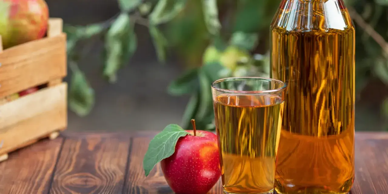 Manzana roja junto a un vaso y botella de vinagre de manzana para limpiar. Cosecha fresca en caja de madera al fondo.
