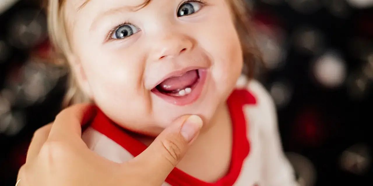 Ein lächelndes Baby mit blauen Augen zeigt stolz seine ersten Zähnchen. Das Baby zahnen ist ein aufregender Meilenstein!