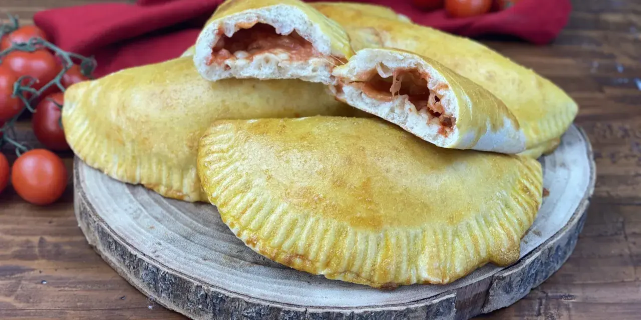 Panzerotti al forno dorati e ripieni di pomodoro e mozzarella filante, pronti per essere gustati.