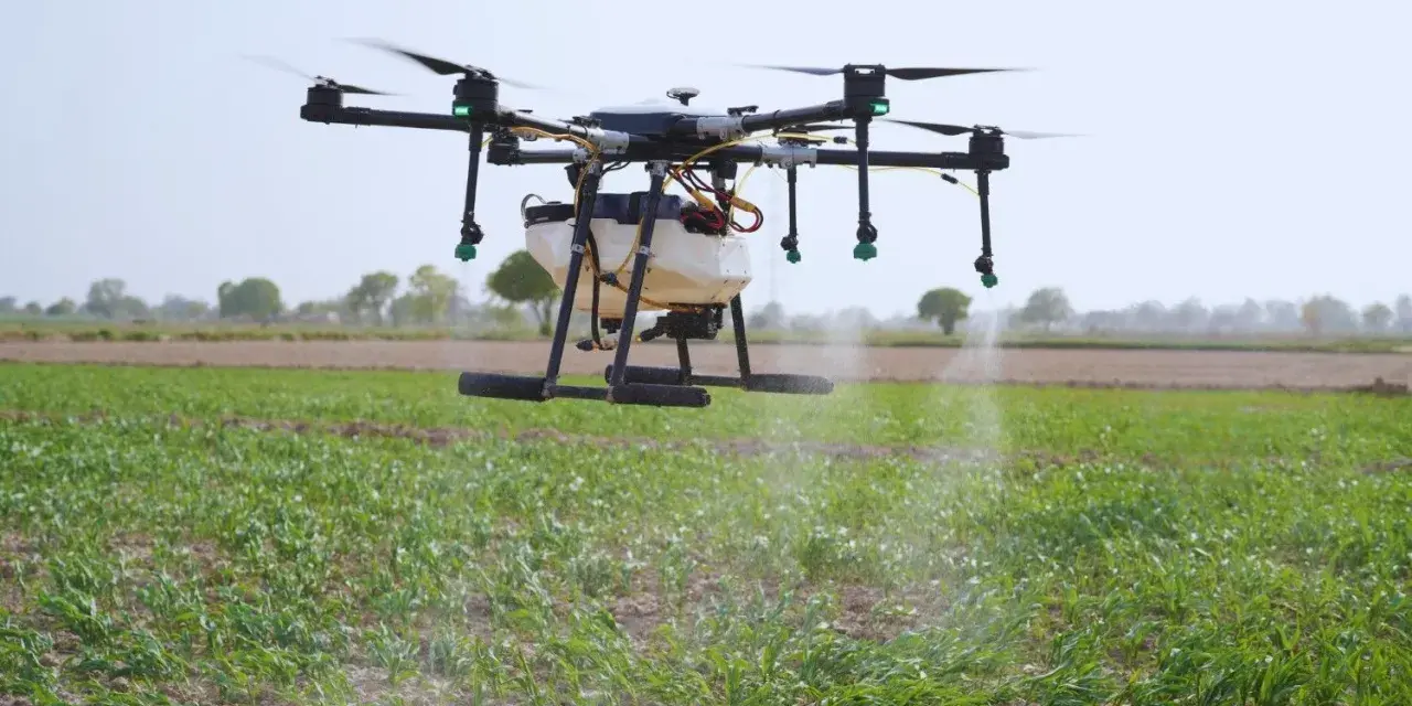 A drone sprayer, one of the types of drones in agriculture, hovers over a field, dispensing liquid onto crops.