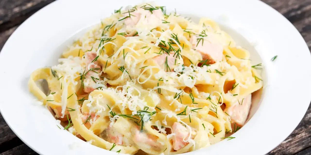 Pyszny makaron z łososiem w kremowym sosie, posypany parmezanem i świeżym koperkiem. Idealny na obiad.