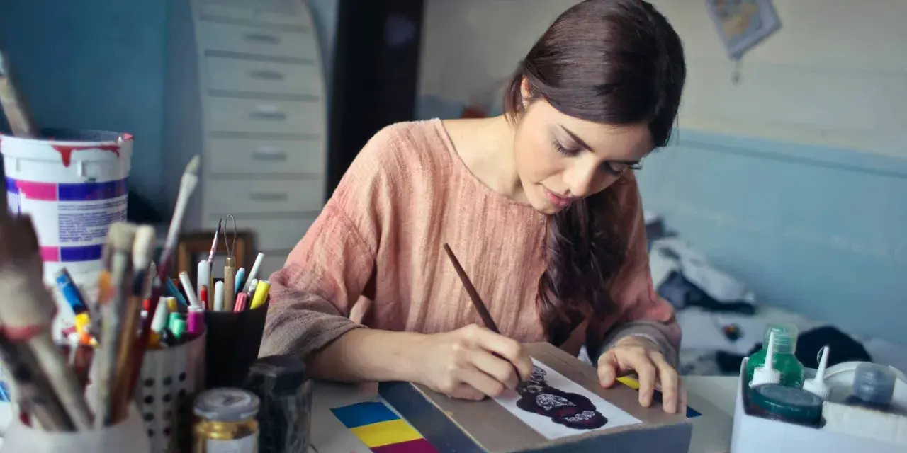 Une jeune femme se déclare artiste libre, concentrée sur sa toile, entourée de pinceaux et de peintures.