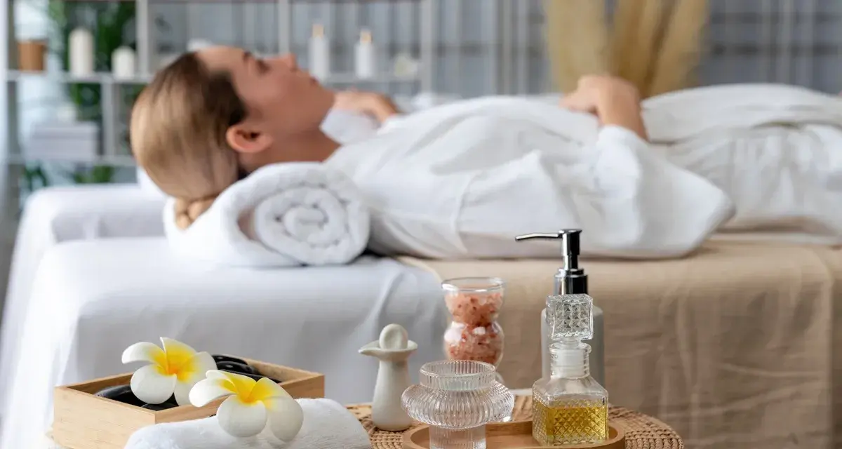 Relaks w jednym z hoteli spa Polska. Kobieta w białym szlafroku leży na łóżku, otoczona kosmetykami i kwiatami.