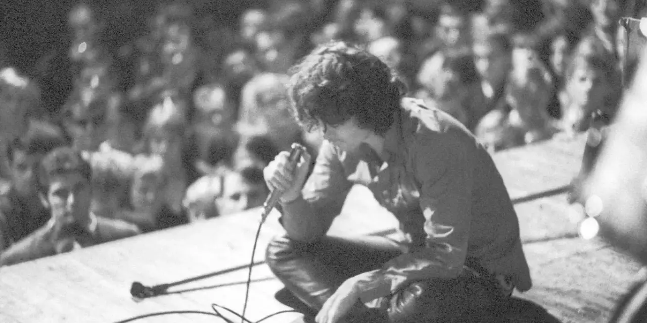 Jim Morrison z The Doors na scenie, wpatrzony w tłum. Jego "Paris Blues" rozbrzmiewa w sercach fanów.
