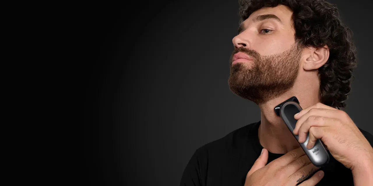 Hombre con barba cola de pato, perfil, usando una recortadora Braun para definir su estilo.