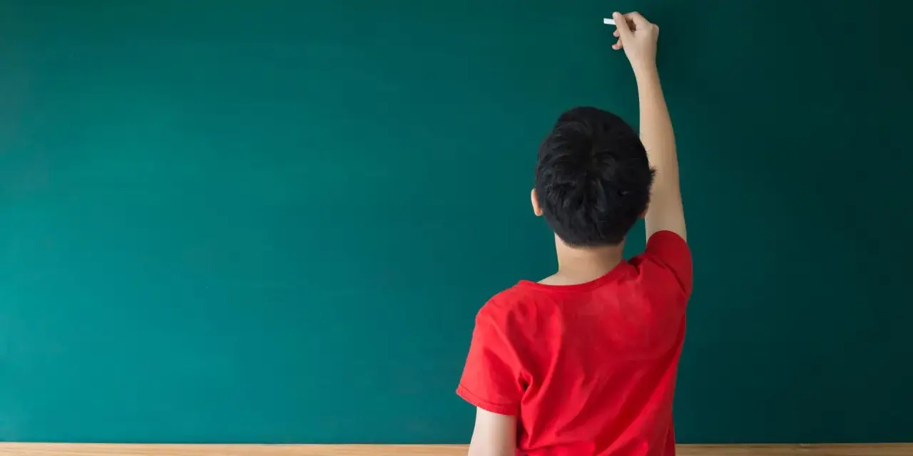 Chłopiec pisze kredą na tablicy, zastanawiając się, przed jakimi spójnikami stawiamy przecinek.